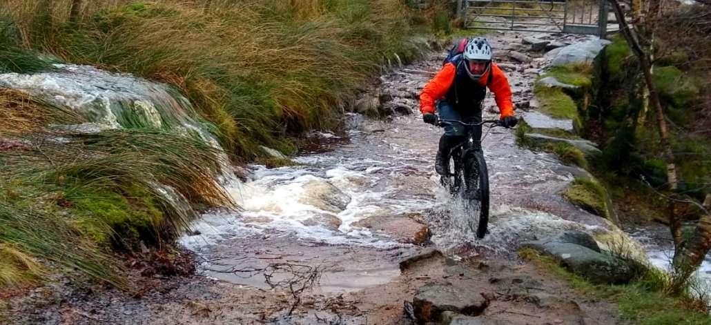 a mountain biker riding through storm water on a cold wet day in the Peak District